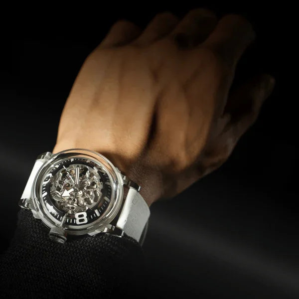 Skeleton mechanical wristwatch with white strap on wrist against dark background