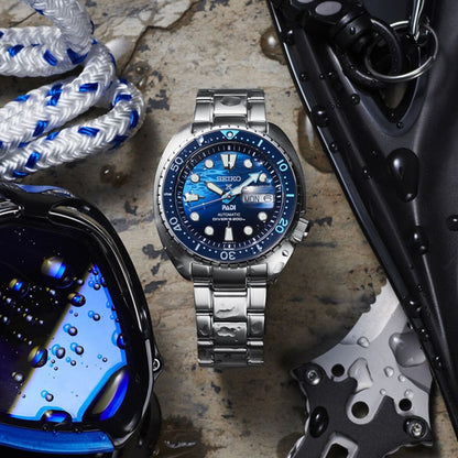 Stainless steel dive watch with blue dial, surrounded by water droplets, rope, goggles, and diving gear.