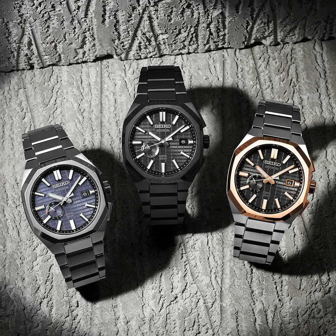 Three modern men's stainless steel watches with textured dials on a stone background