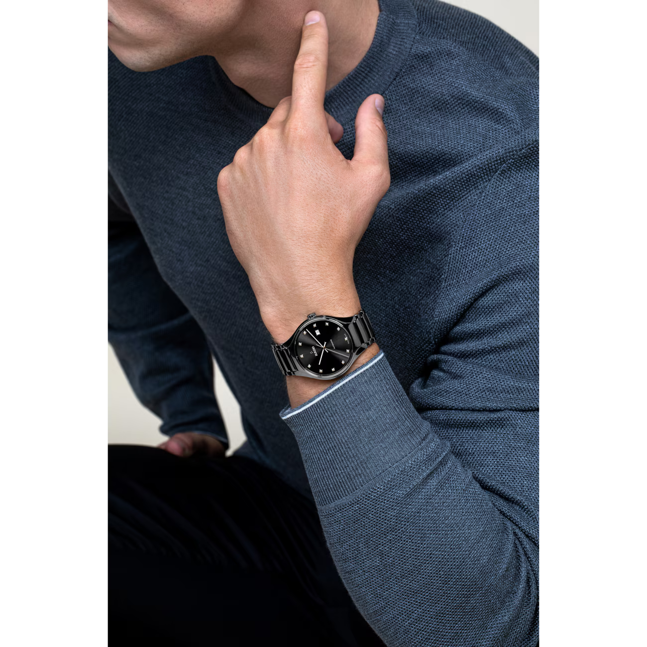 Man met een zwart roestvrijstalen polshorloge met een zwarte wijzerplaat, gekleed in een blauwe trui.