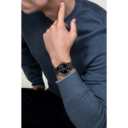 Man met een zwart roestvrijstalen polshorloge met een zwarte wijzerplaat, gekleed in een blauwe trui.